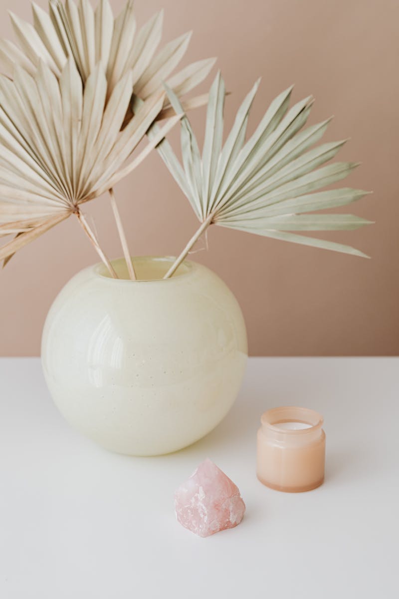 A stylish vase with dried palm leaves and a candle on a white surface.